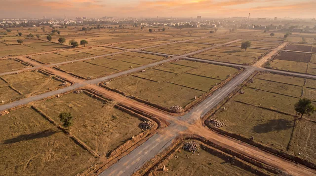 Aerial view at dusk of a grid of unpaved roads laid across empty plotted land, with a city skyline on the horizon.