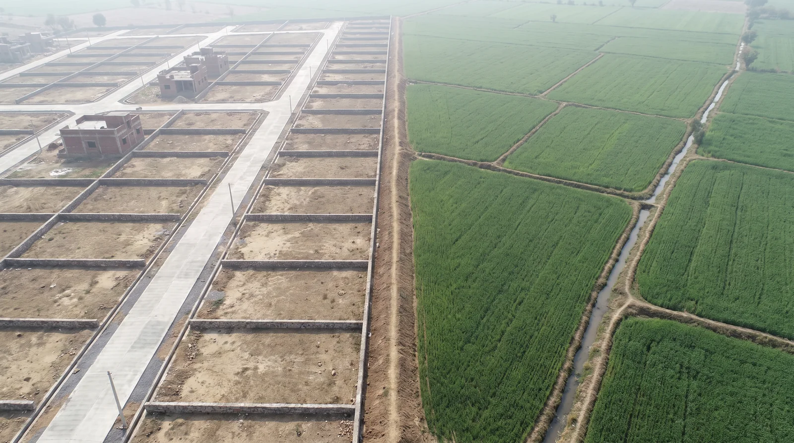 Aerial view of plotted land beside cultivated green fields.