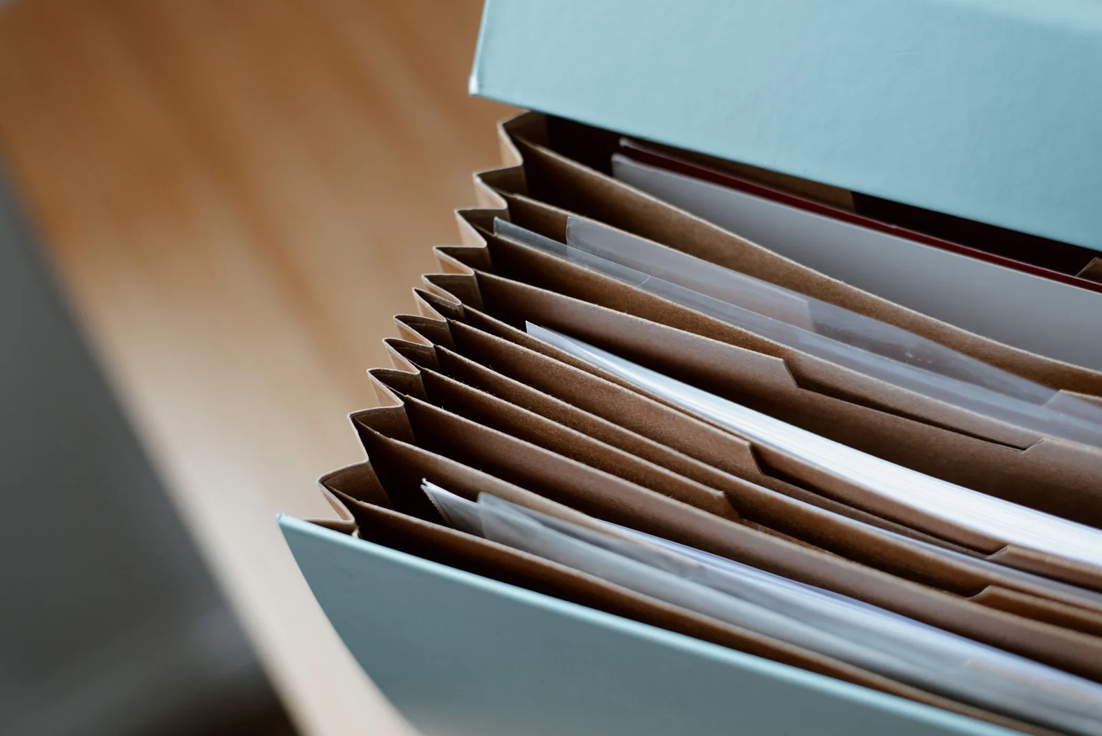 Close view of an open blue-grey expanding file, its brown pockets holding sheets of paper and clear plastic sleeves.