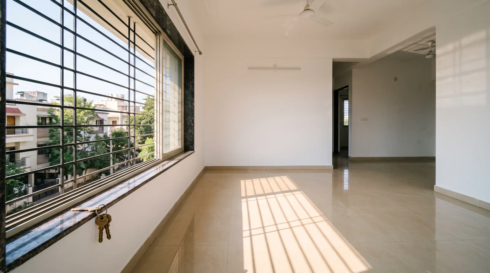 An empty flat with white walls and a glossy beige tiled floor, morning sun falling through a barred window, a ring of brass keys hanging from the window sill.