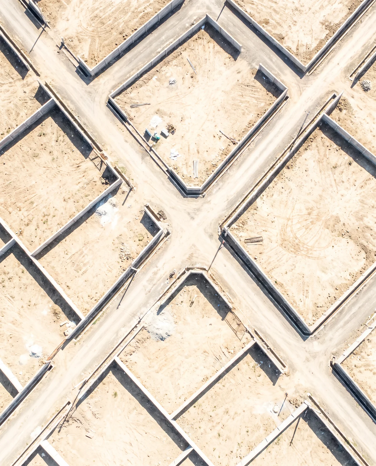 Seen straight down, low walls of empty plots meet at a crossroads of unpaved lanes on dry sandy ground.